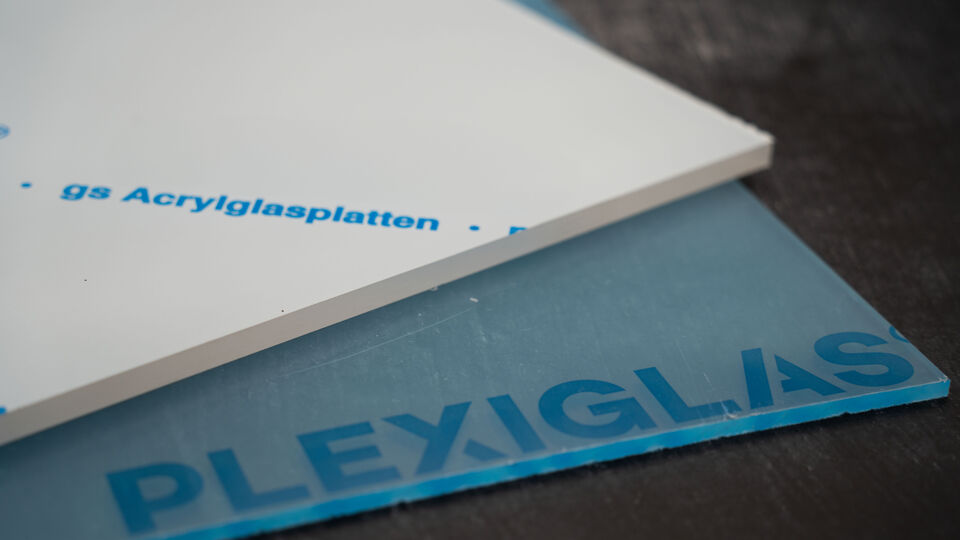 Zwei Acrlyglasplatte der Marke PLEXIGLAS®, weiß und transparent liegen auf einem Tisch